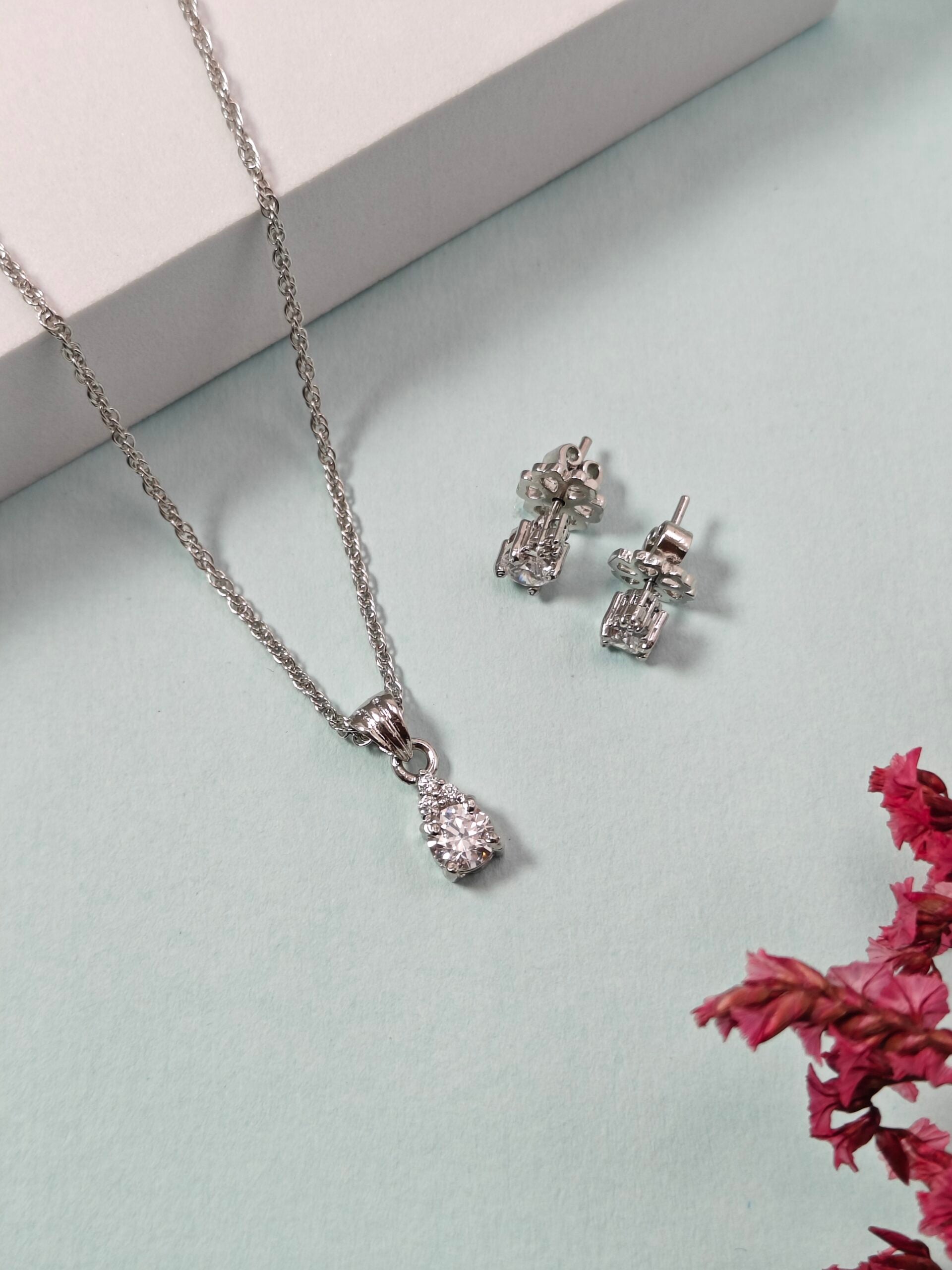 Silver necklace and earrings on a light green surface with pink flowers.